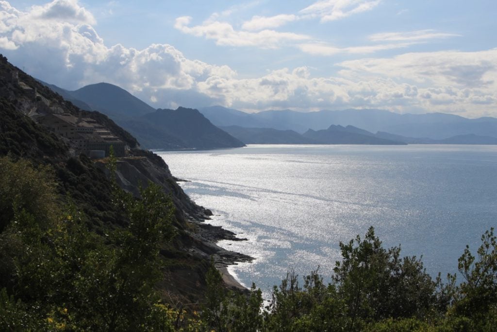 View of coastline in Corsica, with mountains in the distance sunlight shimmering on the sea