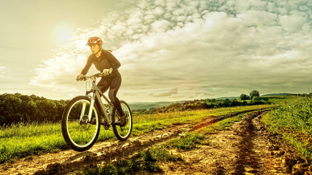 Woman riding a mountain bike along a track through beautiful farmland, in the sunshine
