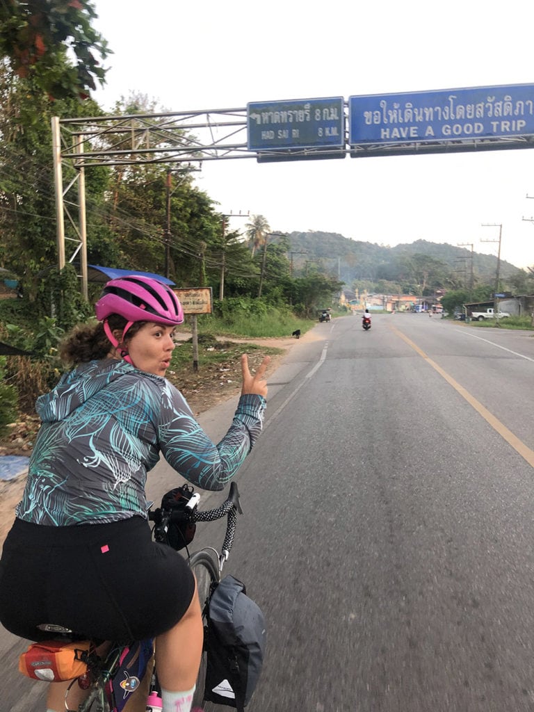 Riding under a bilingual road sign with the message Have a good trip, Thailand