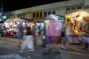 Street scene at a night market, Thailand. Shoppers pass brightly lit stalls.