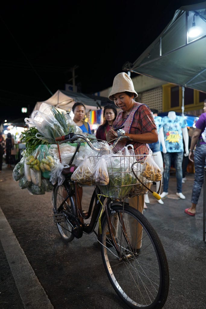 A woman sells vegetables from her bicycle, in a night market in Hua Hin, Thailand