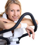 Woman resting on stationary bicycle, smiling while taking a break