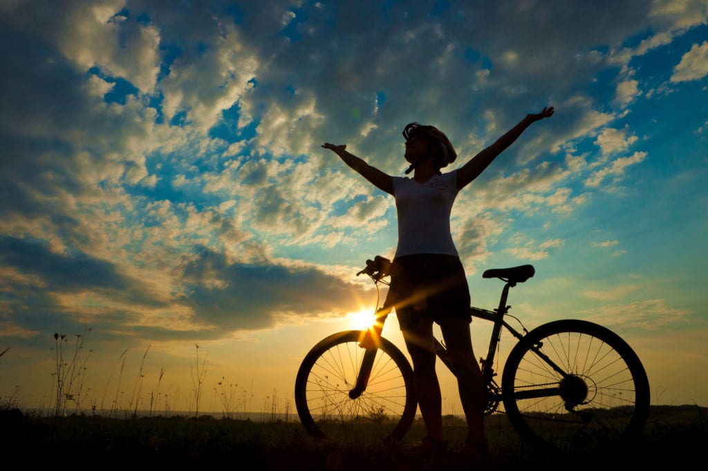 cyclist pauses to celebrate with arms in the air and a beautiful sunset