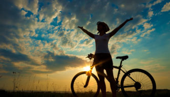 cyclist pauses to celebrate with arms in the air and a beautiful sunset