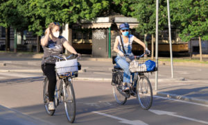 two women cyclists riding in a bike lane wearing face masks