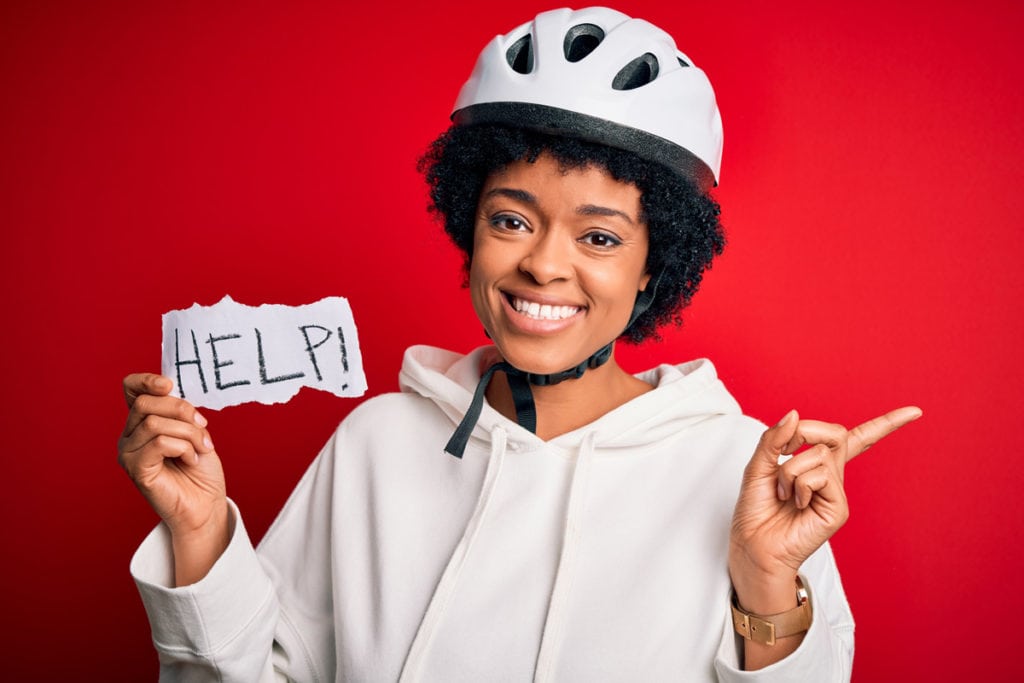 womain in cycling helmet with hand made sign reading help, and text overlayed reading new cyclists welcome here