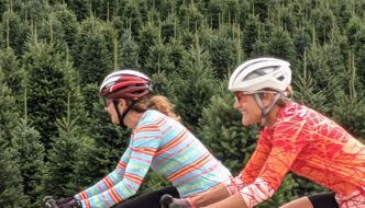 Two women cycling past a christmas tree farm in Vermont