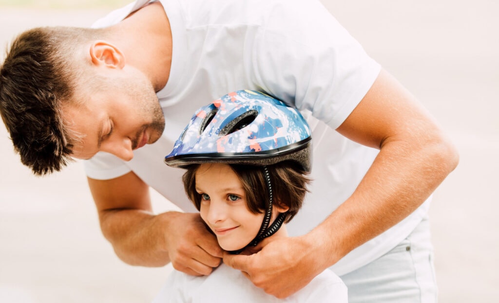 A man securing a bike helmet on a child's head. It does not appear to be sized correctly, and he could use some tips on how to fit a bike helmet properly.