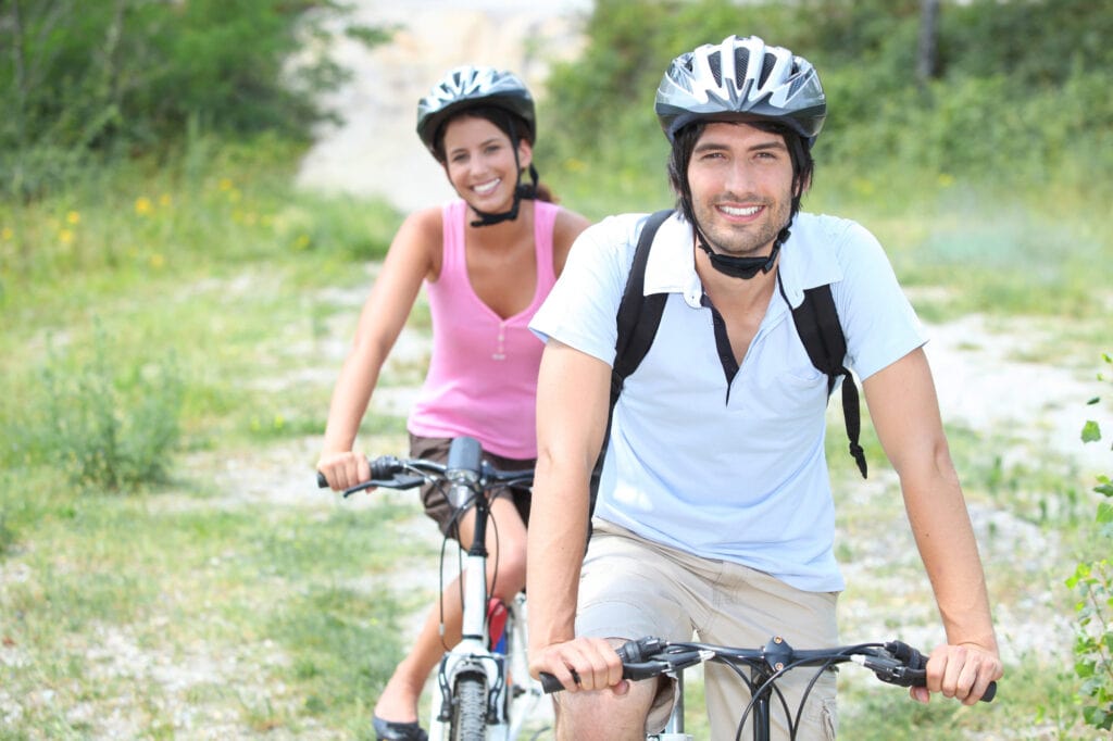 A man and woman wearing bike helmets as they enjoy a bike ride. His is correctly positioned, she needs to learn how to adjust a bike helmet properly.