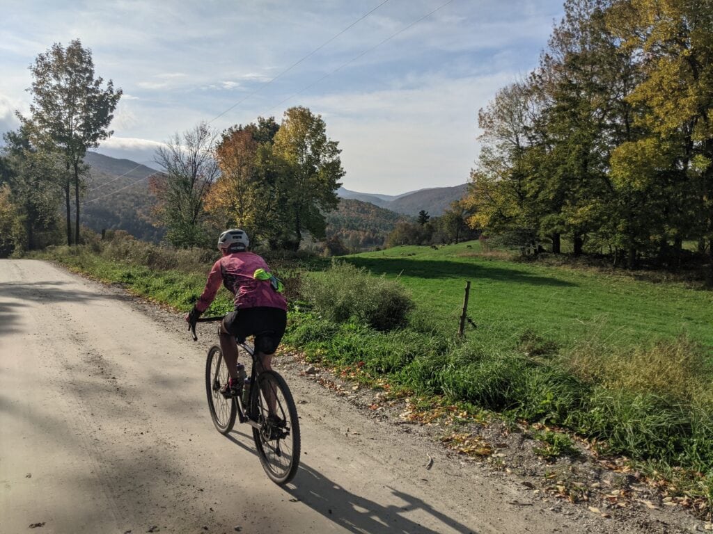 A cyclist riding on a gravel road with a scenic view of Vermont's Fall foliage